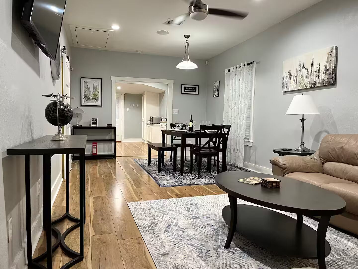 Un salon moderne comprenant un canapé, une table basse, une table à manger et des chaises. Un téléviseur est fixé au mur, un globe se trouve sur une table d’appoint et un tableau est accroché au mur.