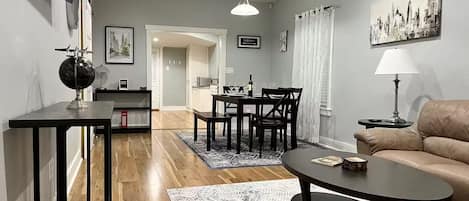 A modern living room with a sofa, coffee table, dining table, and chairs. There is a television mounted on the wall, a globe on a side table, and a painting on the wall.