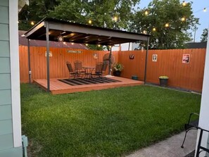 Een achtertuin met een houten terras, een overdekte patio en een verzorgd gazon.