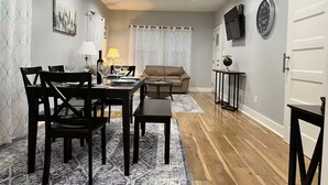 Un coin repas avec une table dressée pour quatre personnes, un canapé, une petite table d’appoint et un ventilateur de plafond.
