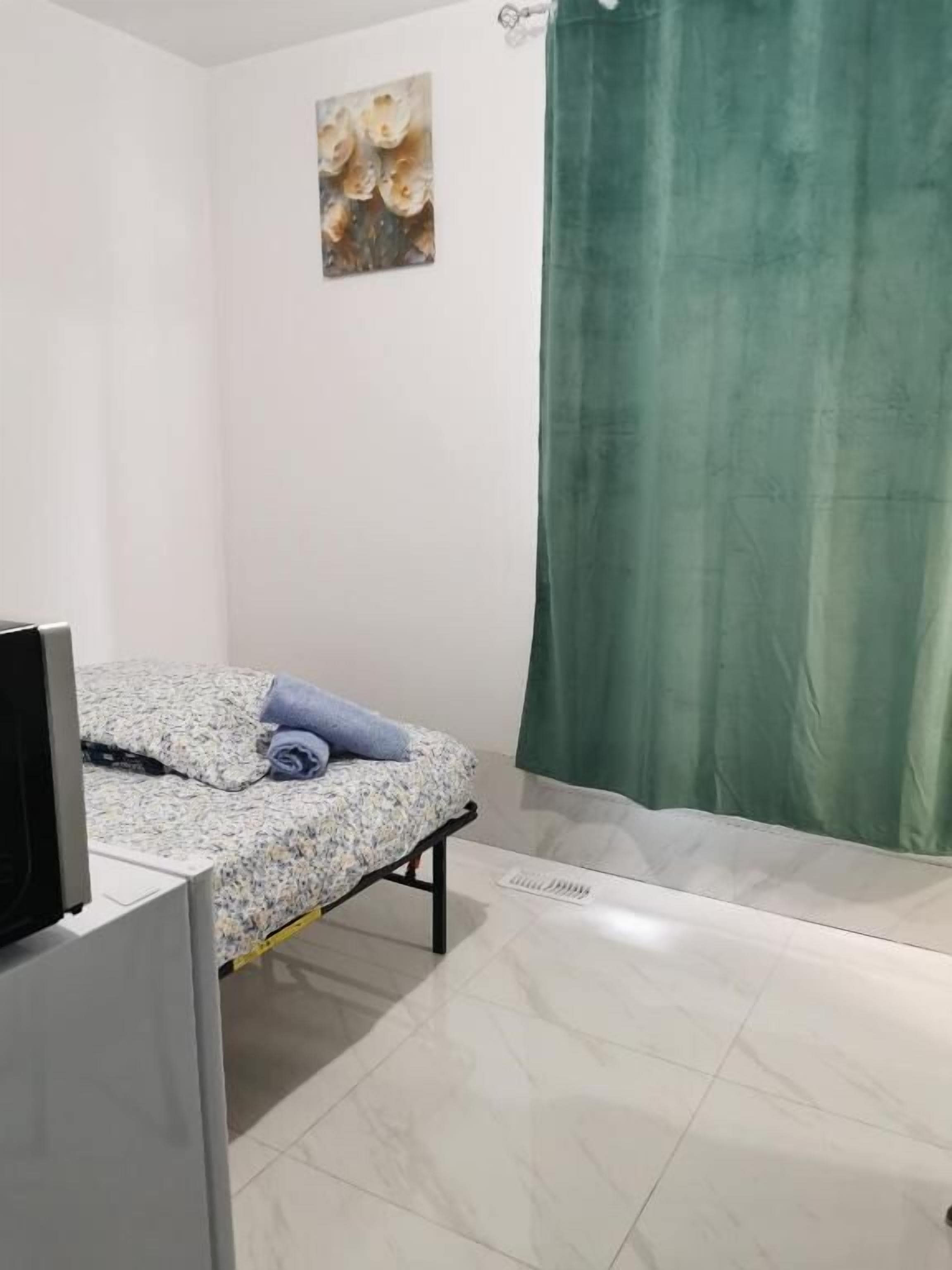 A bedroom with a bed, a television, and a green curtain.