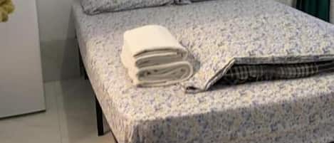 Una cama individual con una colcha estampada, una almohada y una toalla enrollada sobre la cama.