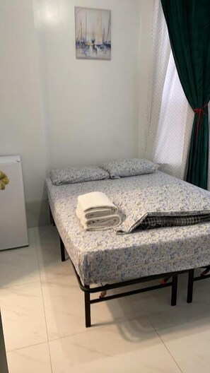 A single bed with a floral bedspread, a pillow, and a rolled towel on the bed.