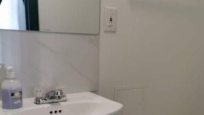 Een badkamer met een witte wastafel, een spiegel, een zeepdispenser en een handgreep.