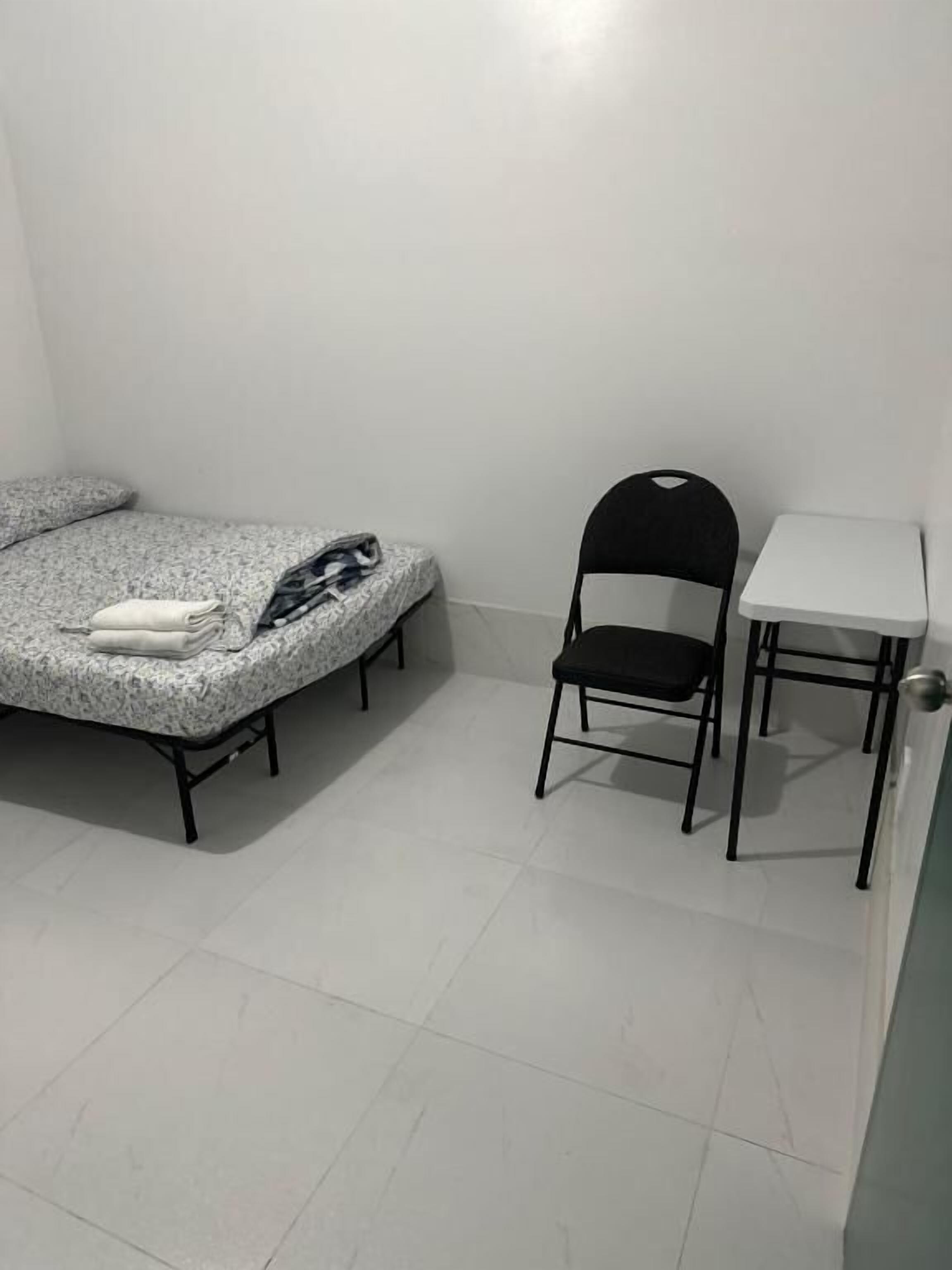 A small, sparsely furnished room with a bed, a chair, and a small table.