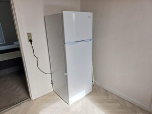 A white refrigerator in a corner of a room with a wooden floor and a white wall. - 2 Person Holiday Home in Vra (Vra)