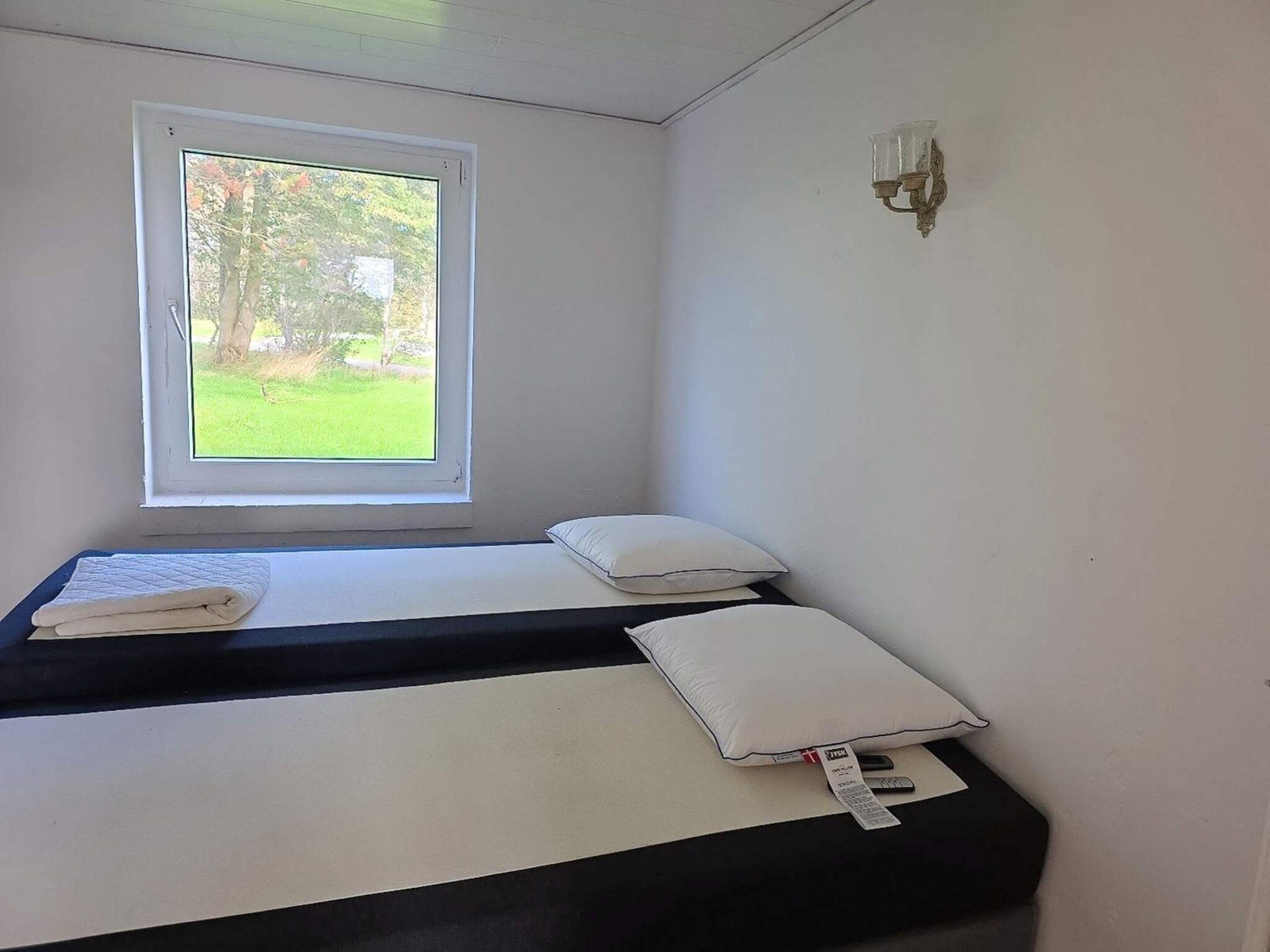 Une petite chambre avec un lit simple et une fenêtre donnant sur un espace verdoyant.