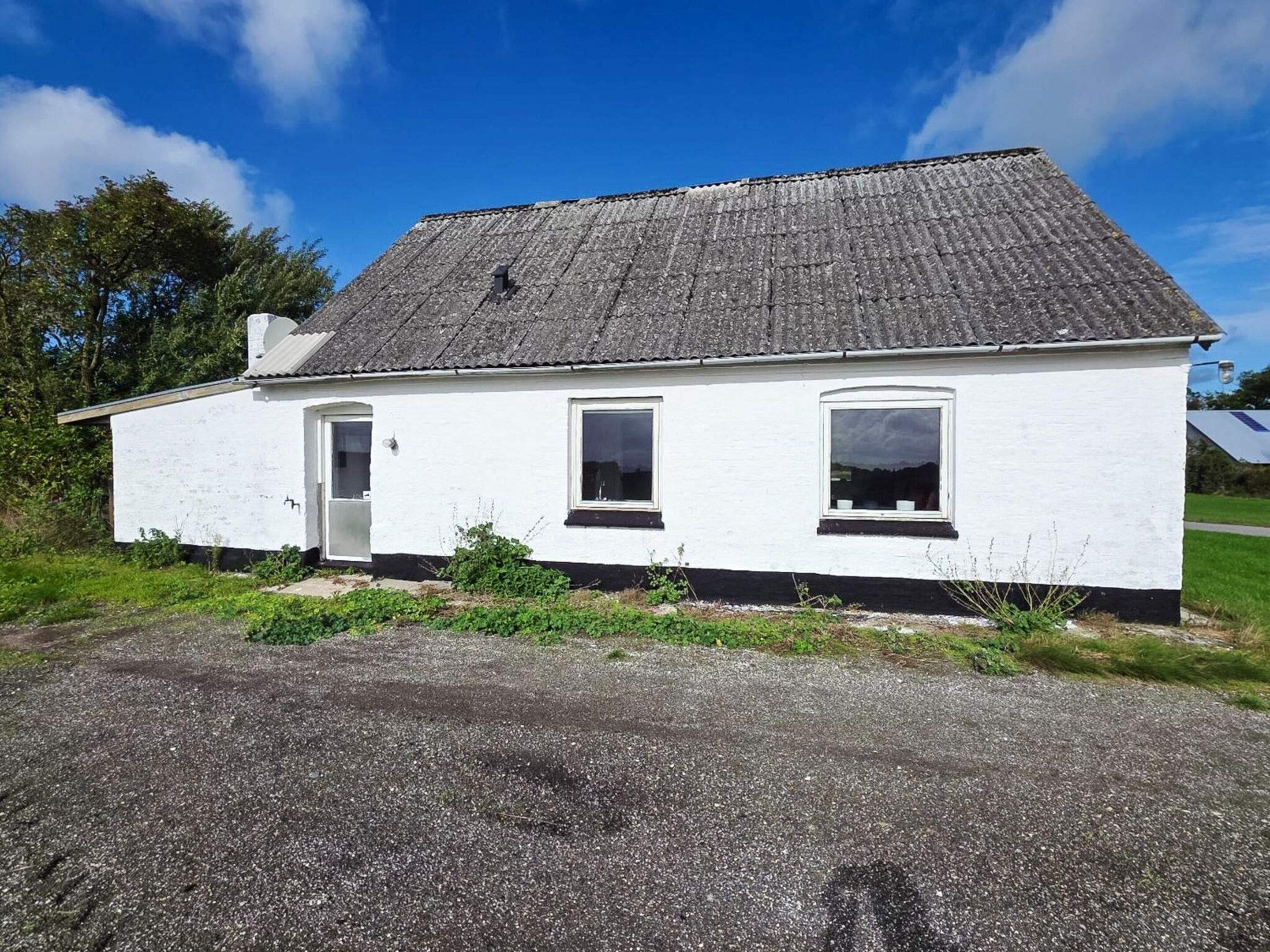 A white single-story house with a grey roof, a door, and two windows.