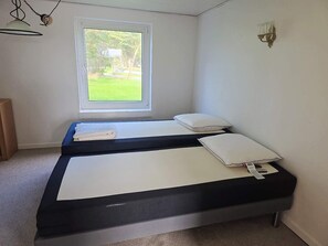 A room with two beds, a window, a wall-mounted light fixture, and a small wooden cabinet. - 2 Person Holiday Home in Vra (Vra)