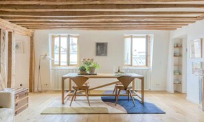 Ein Essbereich mit Holztisch und -stühlen, einer Topfpflanze und Blick durch offene Fenster.