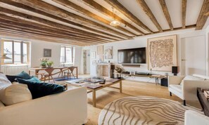 Ein großzügiges Wohnzimmer mit Holzboden, einem an der Wand befestigten Flachbildfernseher und einem Essbereich mit Tisch und Stühlen.