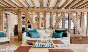 A cozy living room with a white sofa, teal cushions, a chessboard, and exposed wooden beams. - A TRULY PARISIAN CHARM – WHERE HISTORY MEET LUXURY – PONT DE ARTS –SAINT GERMAIN (Paris)