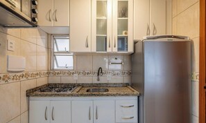 Una cocina con armarios blancos, un refrigerador de acero inoxidable, una estufa a gas y una ventana con vistas.