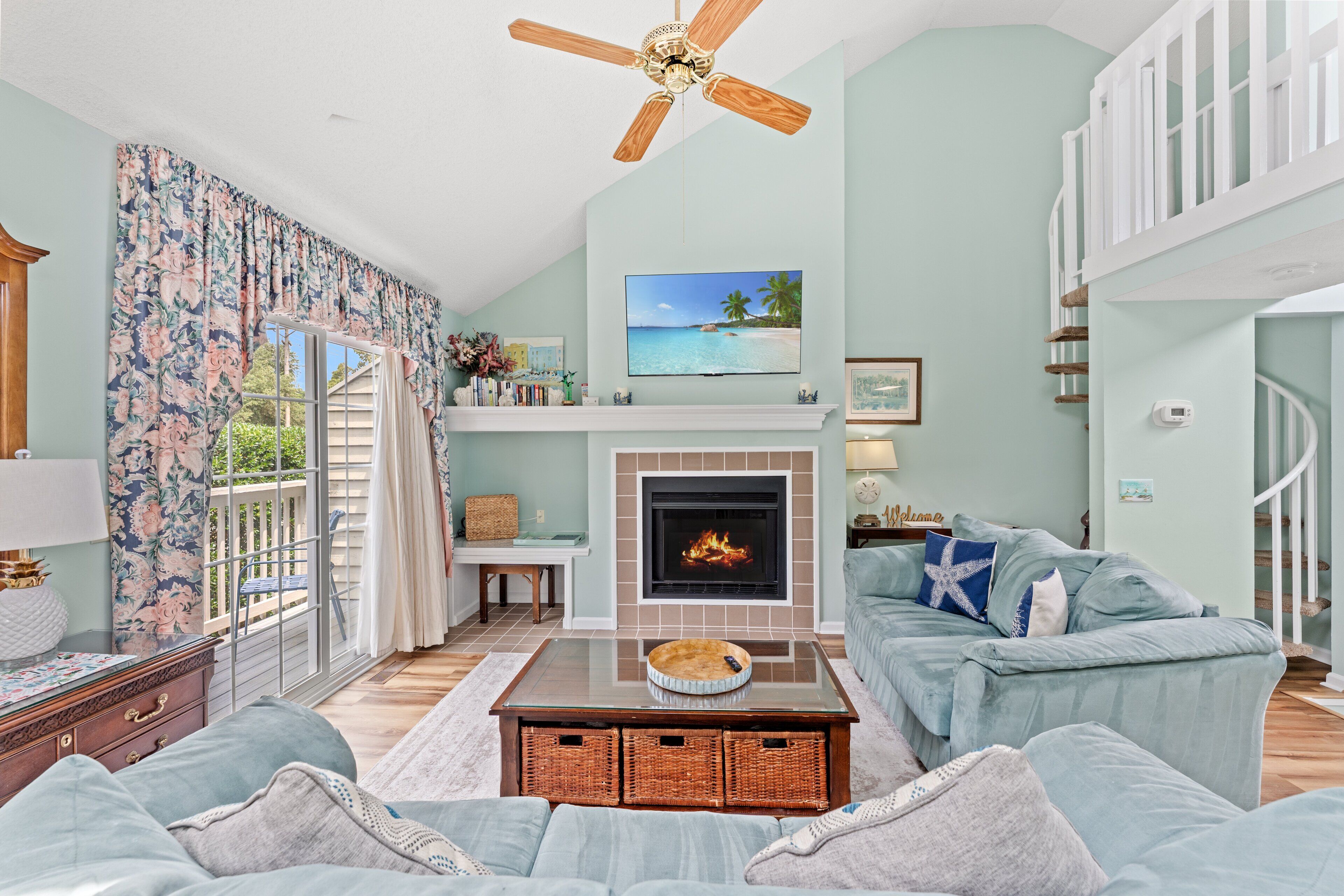 A living room with a fireplace, a ceiling fan, a sofa, and a television.