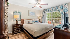 A bedroom with a bed, a ceiling fan, a TV, a dresser, a nightstand, and a window with a view. - Cumberland Terrace 2E (Myrtle Beach)