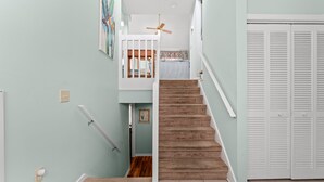 A staircase with a carpeted landing, a white railing, and a door with louvered shutters. - Cumberland Terrace 2E (Myrtle Beach)