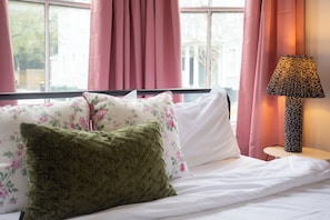 A neatly made bed with floral and green pillows, a bedside lamp, and pink curtains. - Savannah Home, Walkable to Forsyth, Historic (Savannah)
