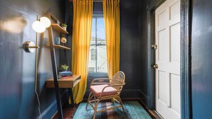 Ein Zimmer mit Holzstuhl, Schreibtisch mit Büchern und Pflanze, Fenster mit gelben Vorhängen und einer Tür.