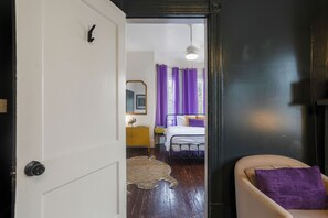 Een slaapkamer met een bed, paarse gordijnen, een spiegel en een gele dressoir.
