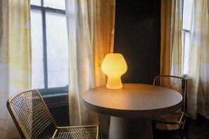 A round table with a lamp, two wireframe chairs, and a window with curtains. - 2 bed/1 bath, Walkable to Forsyth, Historic (Savannah)