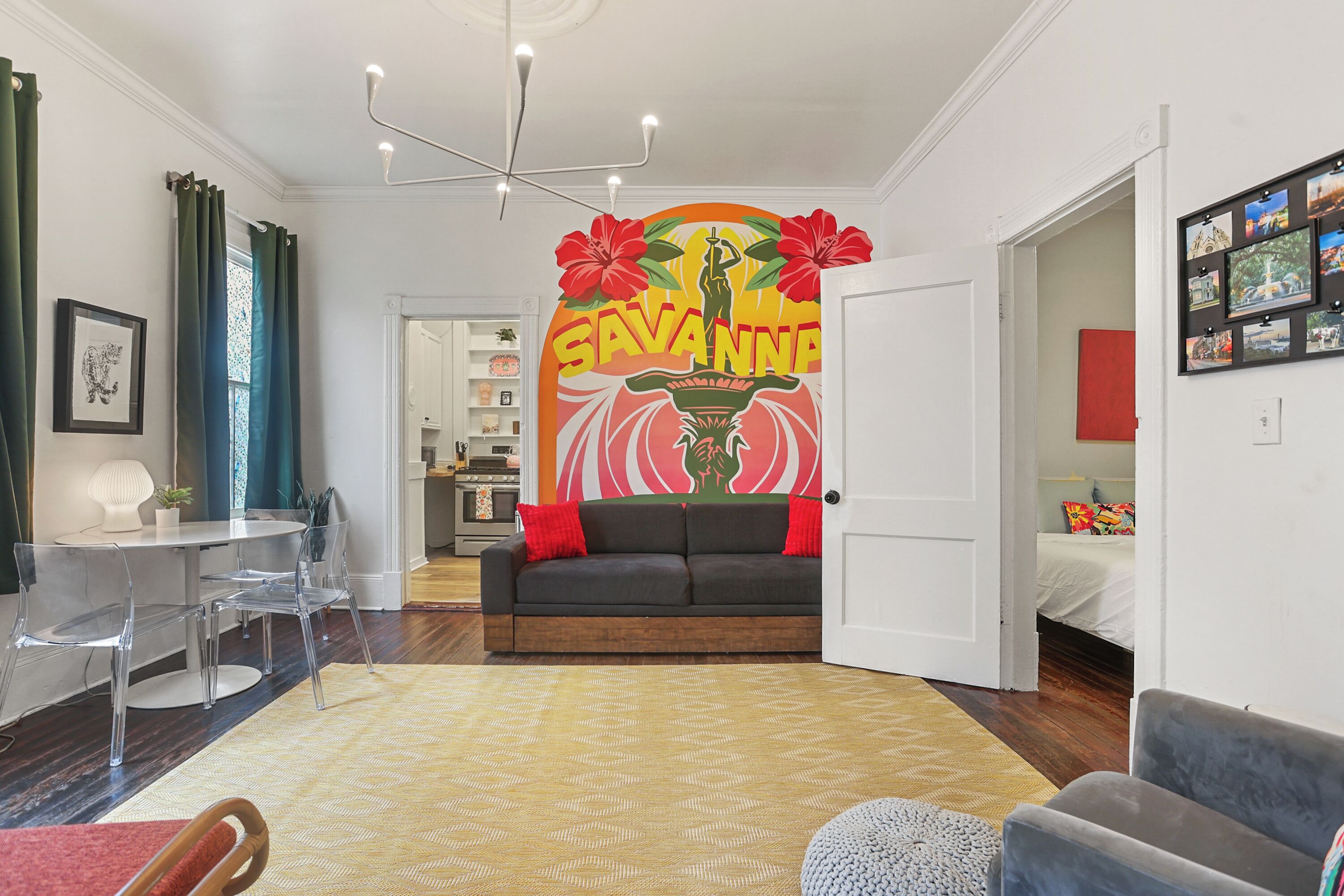 A living room with a sofa, a dining table with chairs, a coffee table, and a wall with a mural.