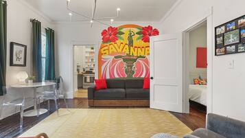 A living room with a sofa, a dining table with chairs, a coffee table, and a wall with a mural.