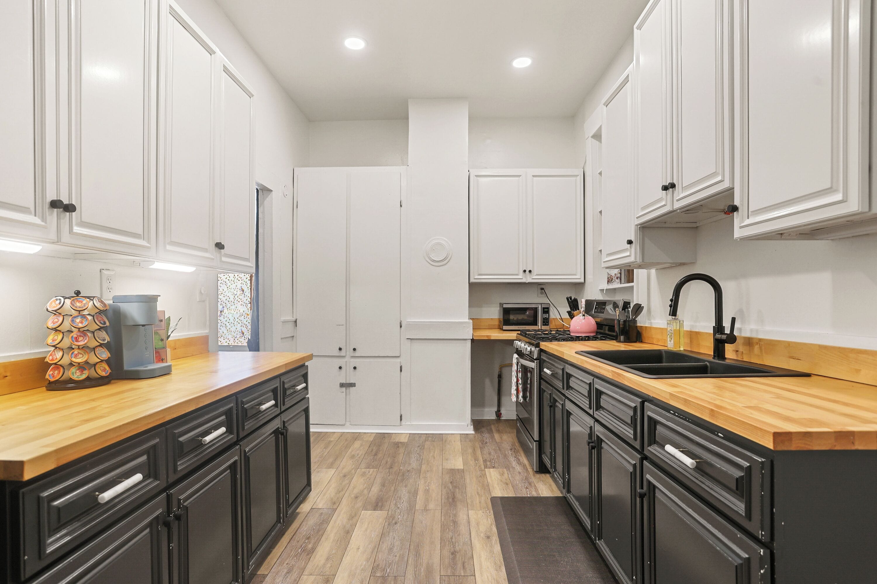 A modern kitchen with white cabinets, black countertops, and a wooden floor.