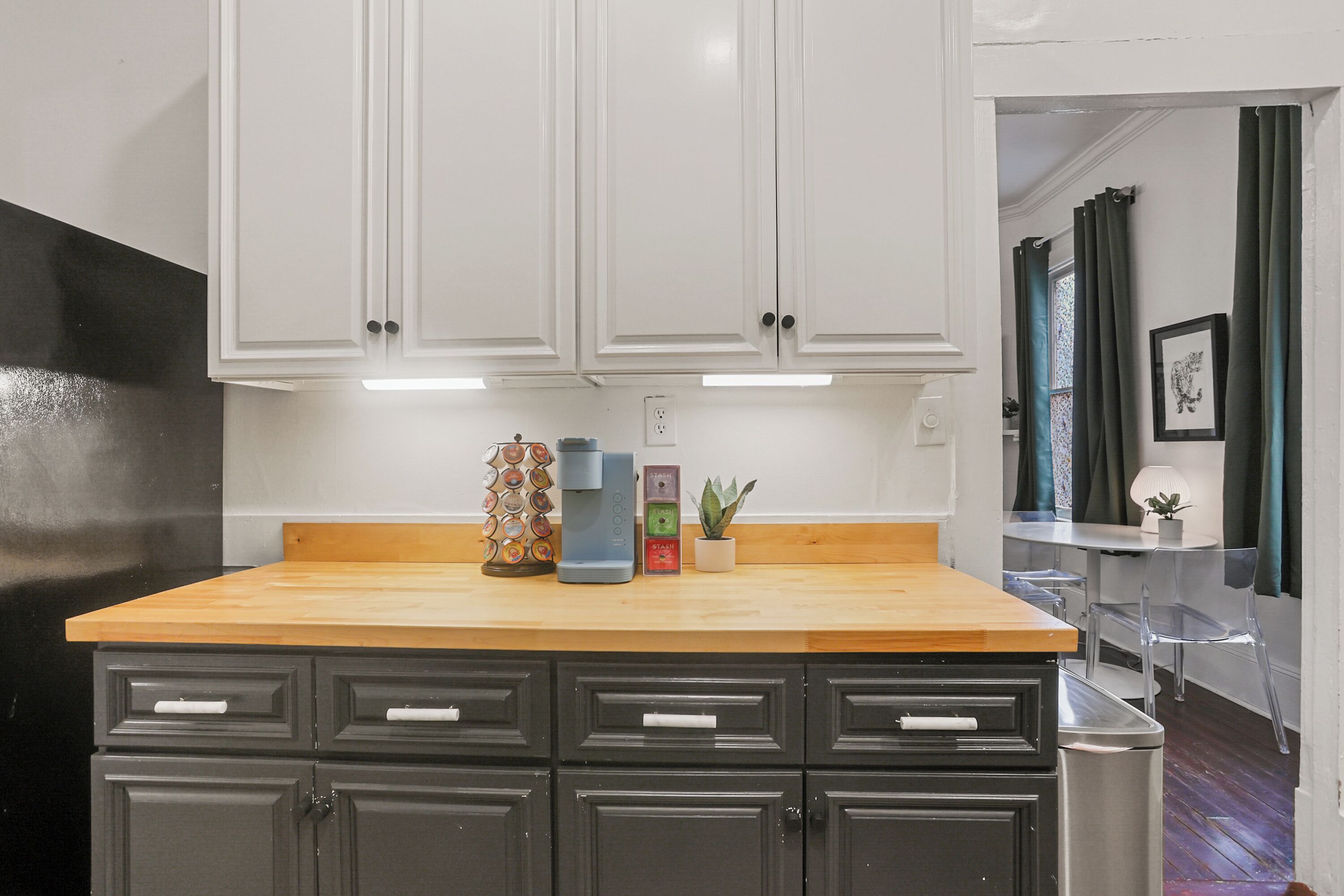 Una cocina con armarios blancos, encimera de madera y un cubo de basura.