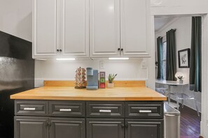 Una cocina con armarios blancos, encimera de madera y un cubo de basura.