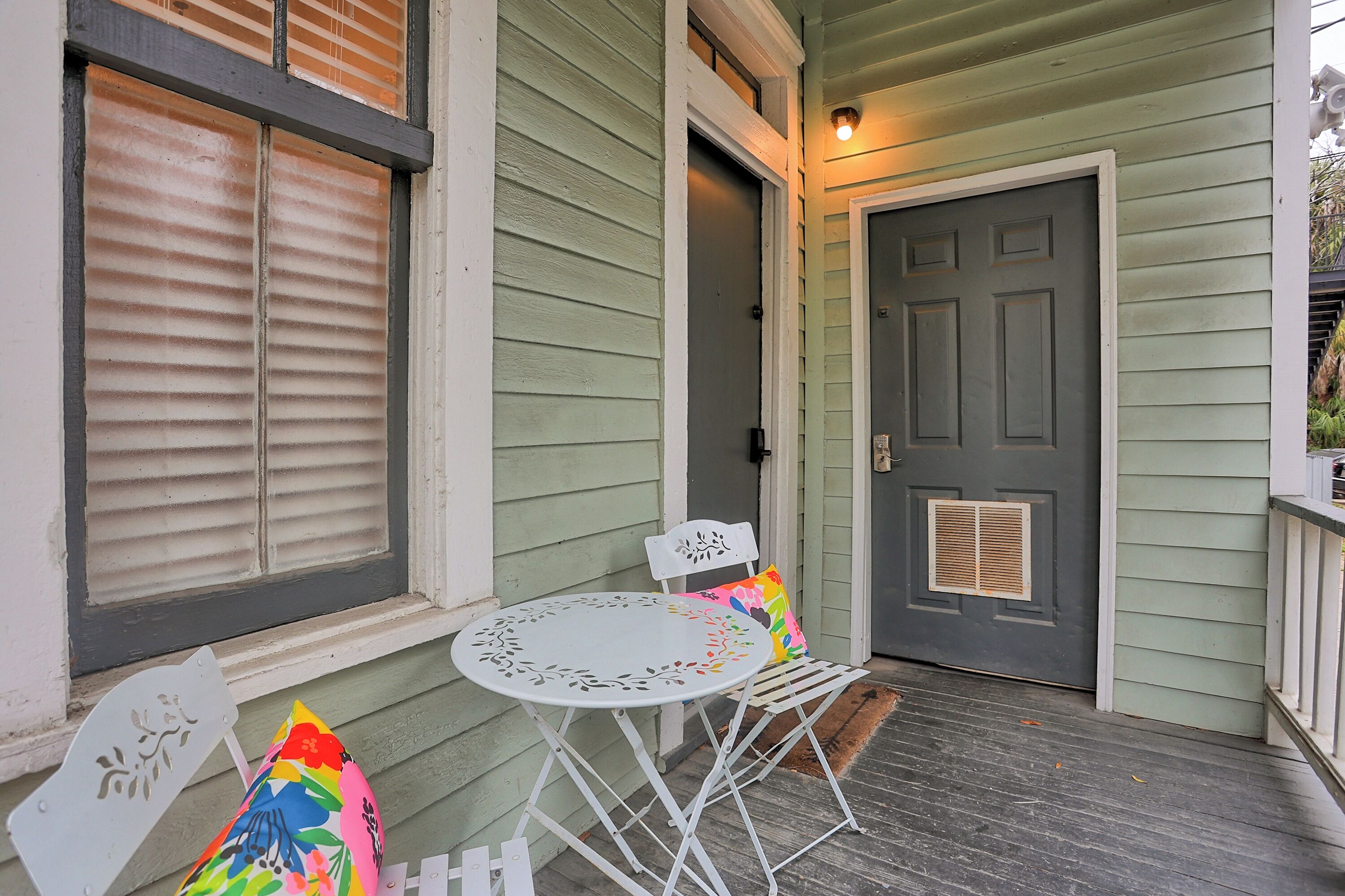 A porch with a white metal table and chairs, a gray door, and a window with blinds.
