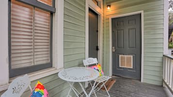 A porch with a white metal table and chairs, a gray door, and a window with blinds.