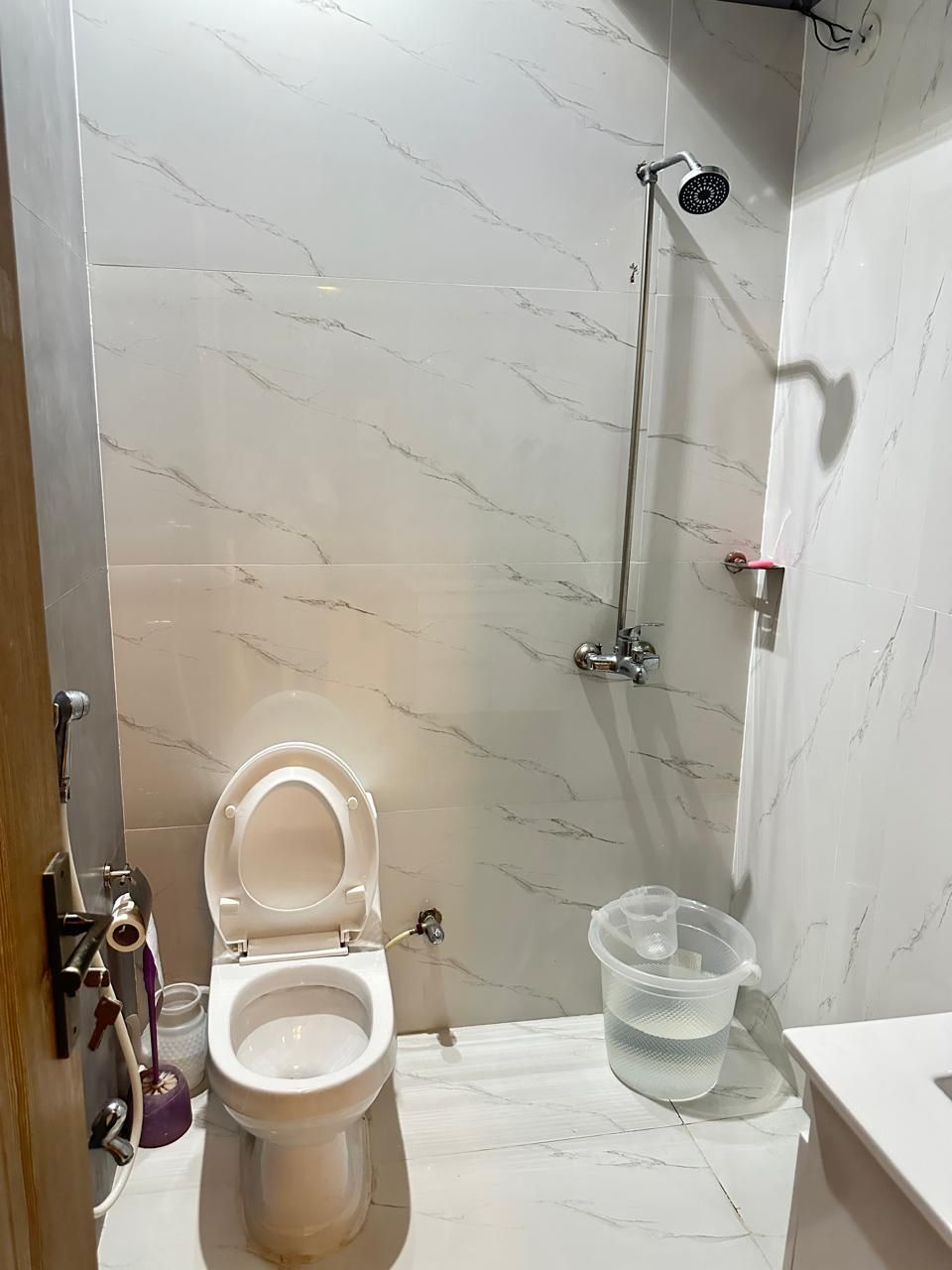 A bathroom with a toilet, shower, and a clear plastic water container.