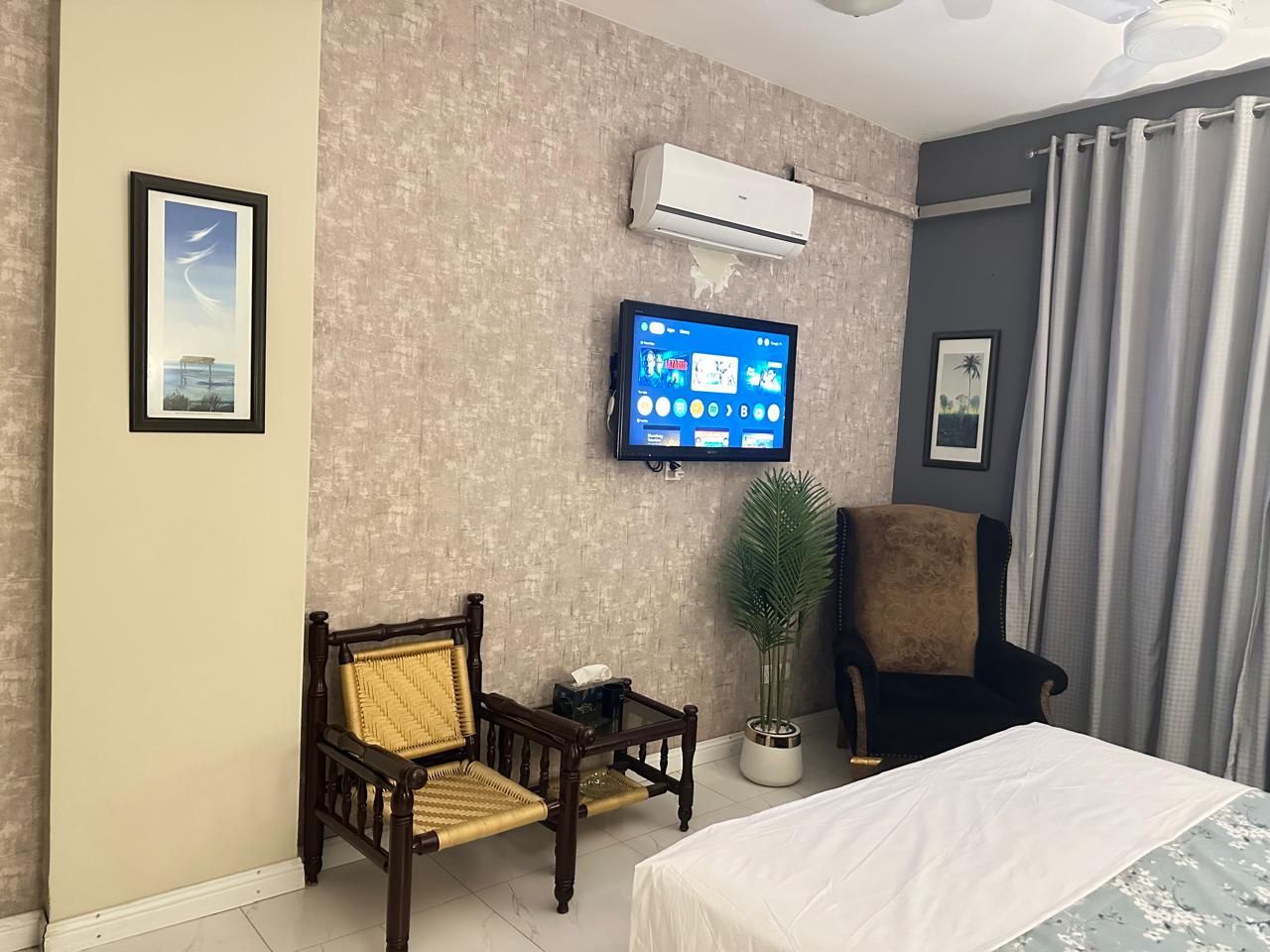 A hotel room with a bed, two chairs, a television, and a potted plant.