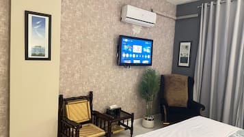 A hotel room with a bed, two chairs, a television, and a potted plant.