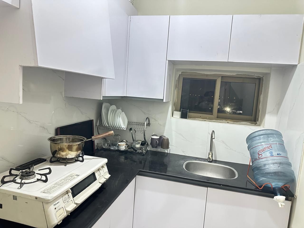 A compact kitchen with white cabinets, a gas stove, a sink, and a window above the sink.