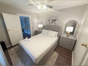 A bedroom with a bed, bedside tables, a mirror, a world map on the wall, and a ceiling fan. - Newly Remodeled Oasis - Fast WiFi + Vit C Shower + Free Parking (Houston)