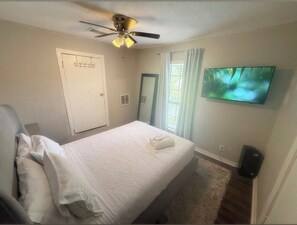 A hotel room with a bed, a ceiling fan, a television, and a door. - Newly Remodeled Oasis - Fast WiFi + Vit C Shower + Free Parking (Houston)