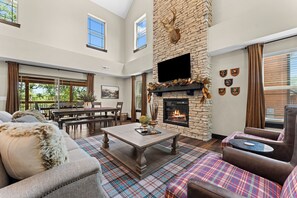 A spacious living room with a stone fireplace, a dining area, and a large window. - 4 Ensuite Baths | Hot Tub | Pool + Lazy River (Hollister)