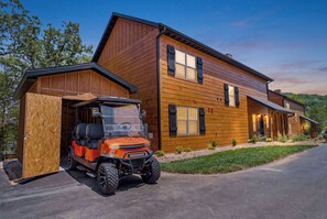 Ein zweistöckiges Holzhaus mit einer überdachten Garage und einem großen, orangefarbenen Geländewagen davor.