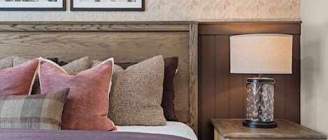 A neatly made bed with a variety of pillows, a bedside lamp, and a wall with floral wallpaper.