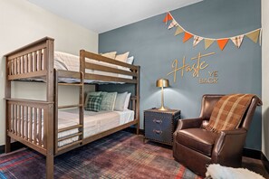 Ein Stockbett mit einer Kommode und einem Ledersessel in einem Zimmer mit kariertem Teppich.