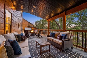 A covered outdoor seating area with a fire feature, wooden deck, and a view of trees. - 4 Ensuite Baths | Hot Tub | Pool + Lazy River (Hollister)
