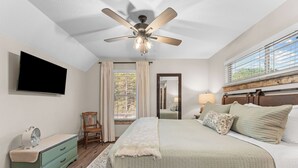 A bedroom with a bed, a ceiling fan, a TV, a dresser, a chair, and a window with curtains. - Oak-Zarks Getaway - Cabin w/ 2 King Suites, Hot Tub, Fire Pit + Resort Amenities (Hollister)