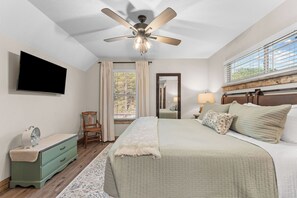 A bedroom with a bed, a ceiling fan, a TV, a dresser, a chair, and a window with curtains. - Oak-Zarks Getaway - Cabin w/ 2 King Suites, Hot Tub, Fire Pit + Resort Amenities (Hollister)