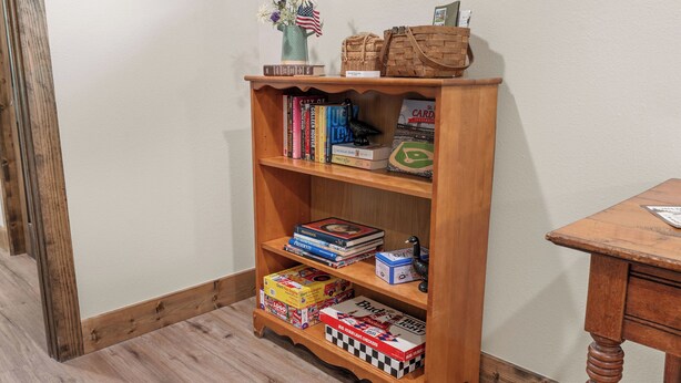 A wooden bookshelf with books, a vase with flowers, and a small American flag. - Oak-Zarks Getaway - Cabin w/ 2 King Suites, Hot Tub, Fire Pit + Resort Amenities (Hollister)