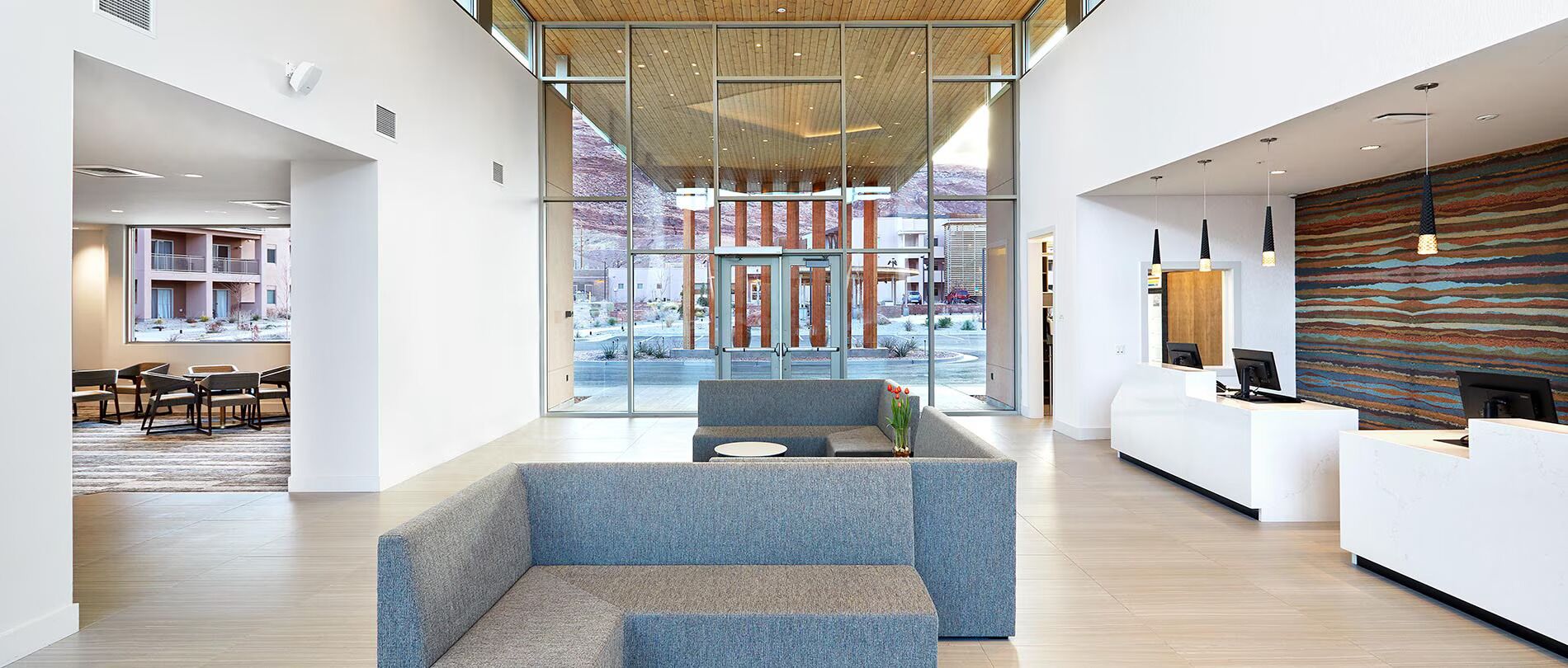 Un hall d’hôtel moderne doté d’un comptoir d’accueil, d’un espace salon et de grandes fenêtres donnant sur l’extérieur.