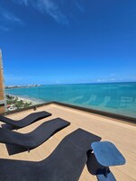 Balcón con sillones de descanso y una mesa, con vista a una playa y el océano.