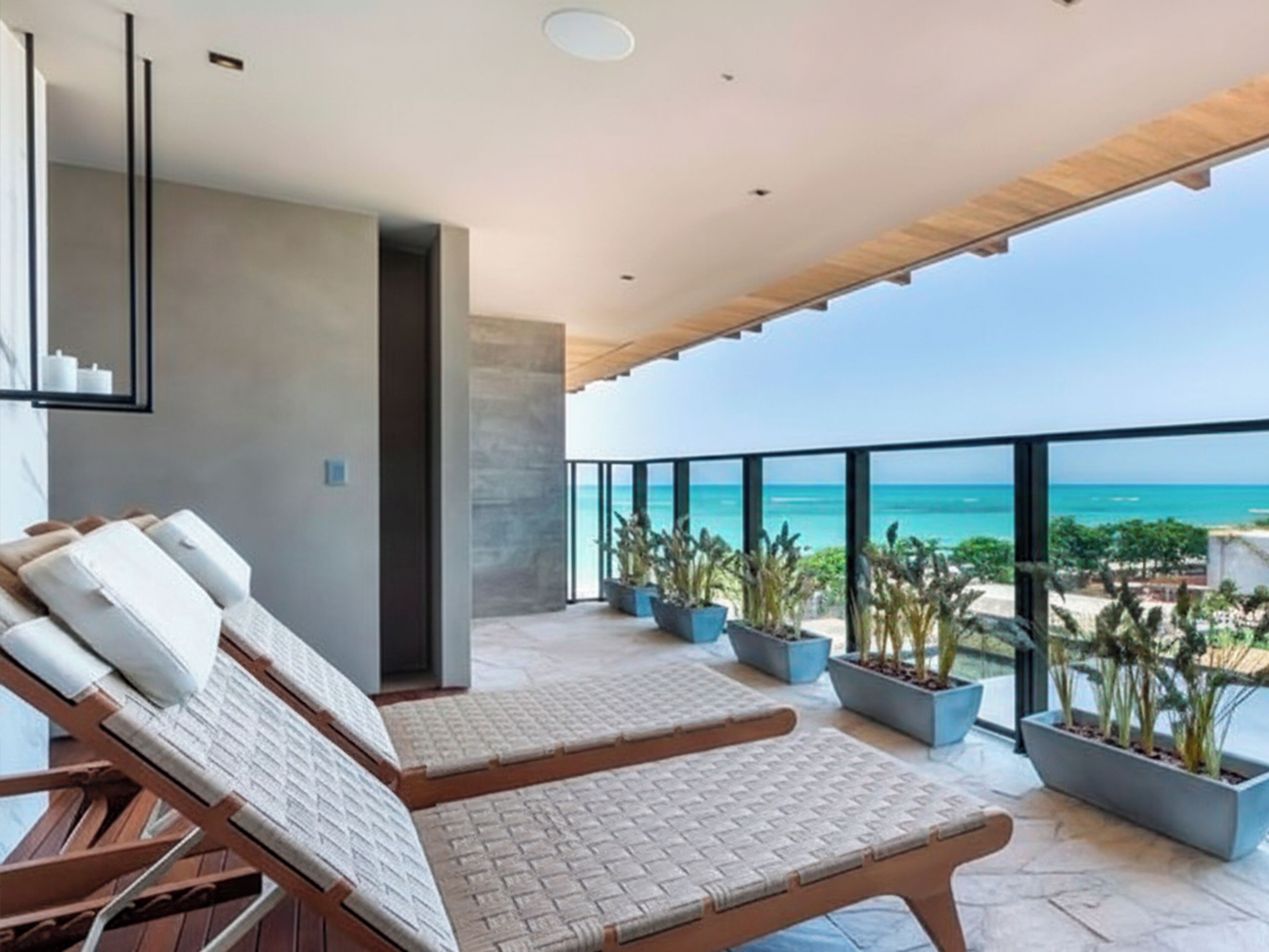 Un balcón moderno con dos sillones de descanso, techo de madera y vista al océano.