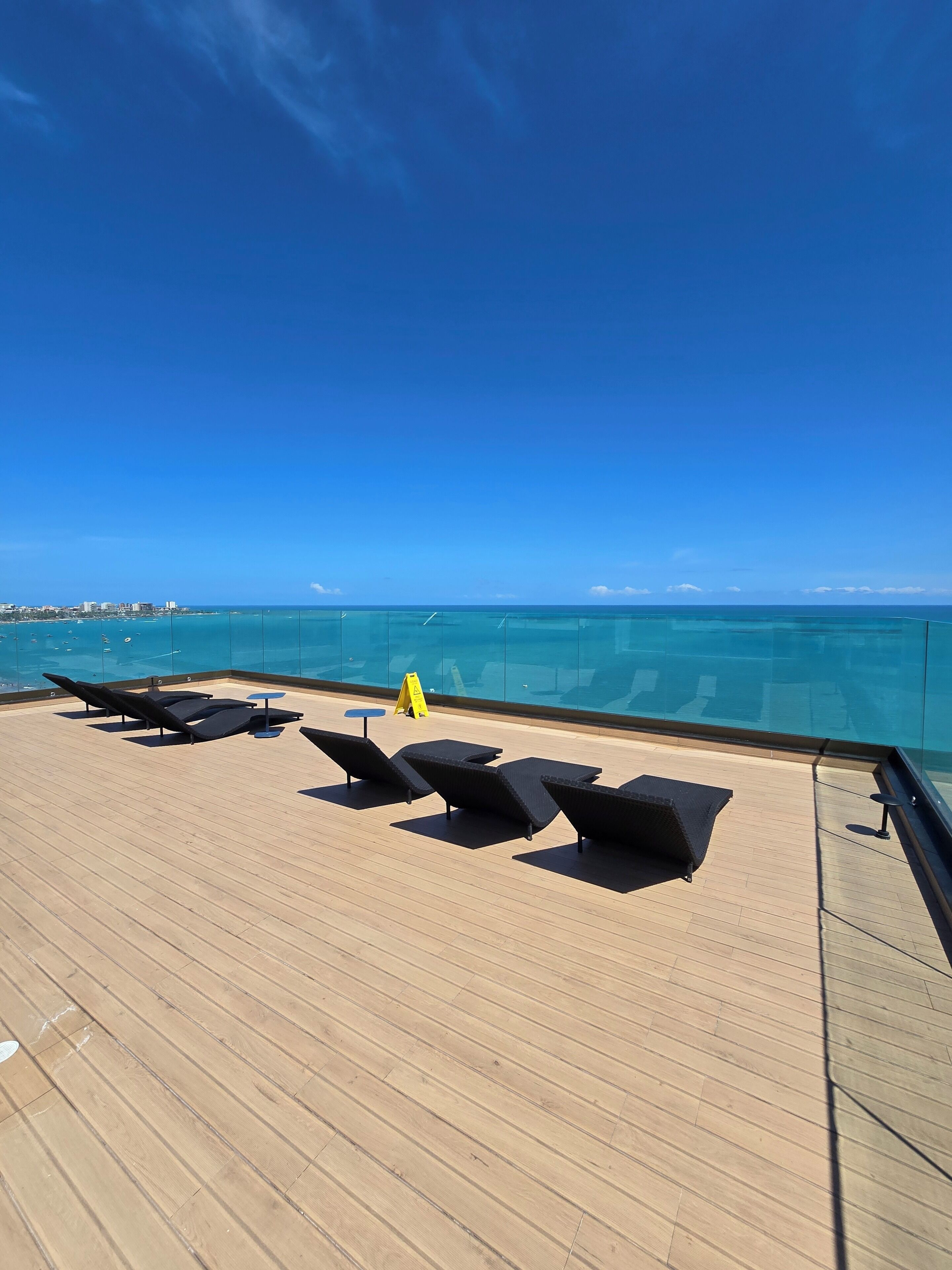 A deck with sun loungers and a glass railing overlooking a clear blue sea.