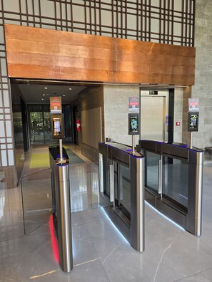A modern hotel entrance with automated turnstiles, a digital information kiosk, and an elevator.